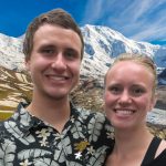 Luke and Teal put their arms around eachother in front of a mountain valley.