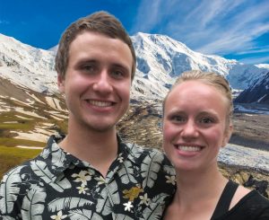 Luke and Teal put their arms around eachother in front of a mountain valley.