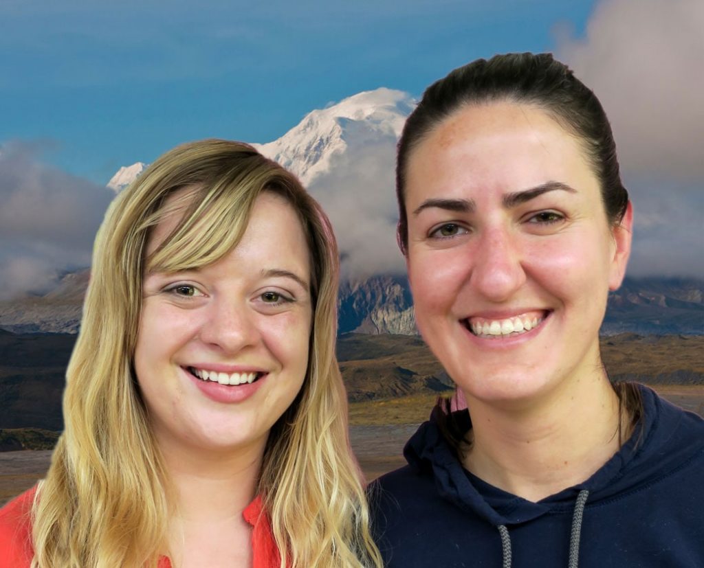Two women stand close together, smiling in front of Denali.