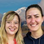 Two women stand close together, smiling in front of Denali.