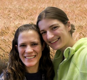Jessiea and Kristin smile at the camera in front of a photoshopped background of a field of grain behind them.
