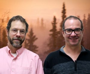 Scott and Bob smile in front of smokey trees.