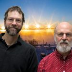 Scott and Terry smile in front of an Alaskan sunrise/sunset timelapse.