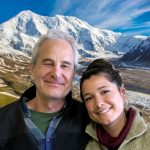 Rick and Naomi put their heads together and smile in front of a mountain and streams.
