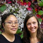 Tonya and Krista smile in front of a bed of lichen and leaves.