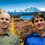 Eran and Gabe smile in front of a lake and mountains.