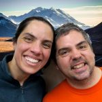 Robert and Rachael lean their heads together and smile in front of a picture of Denali.