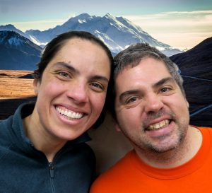 Robert and Rachael lean their heads together and smile in front of a picture of Denali.