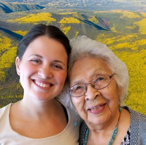 Helen and Stacie a young woman and older woman lean their heads together in front of a vast, hilly forest.