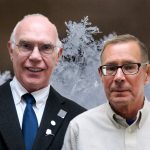 John and Larry, two men with glasses smile in front of a background with close-up snow crystals.