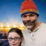 Jeremy and his daughter Merridy smile in front of a bright snowy sunset.