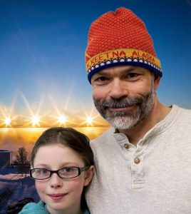 Jeremy and his daughter Merridy smile in front of a bright snowy sunset.