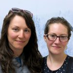 Naomi and Rebecca, two young women, smile in front of snowy trees.