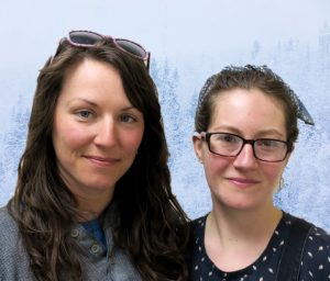 Naomi and Rebecca, two young women, smile in front of snowy trees.