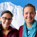 Brooke and Krista smile at the camera in front of a photoshopped background of a snow-covered mountain peak.
