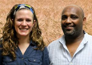 Jessie and Abraham smile at the camera in front of a photoshopped background of a grain field.