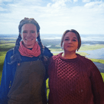 Two women smile in front of a photoshopped background of a vast swampy tundra.